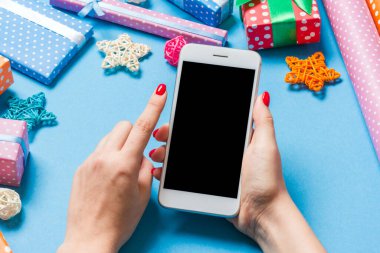 Neşeli mavi arka planda kadın elinin telefonunun üst görüntüsü. Noel süsleri. Yeni yıl tatili. Model.