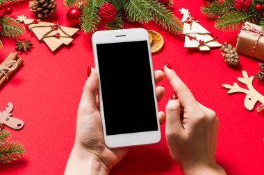 Kırmızı arka planda bayanların telefonunun üst görüntüsü. Noel süsleri. Yeni yıl tatili. Model.