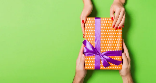 Top view of giving and receiving a present on colorful background. A man and a woman holding gift in hands. Festive concept with copy space.