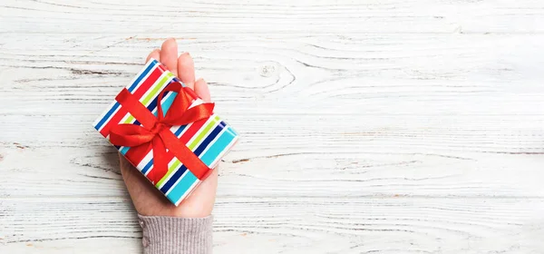 Woman hands give wrapped christmas or other holiday handmade present in colored paper . Present box, decoration of gift on white rustic wooden table, top view with copy space.