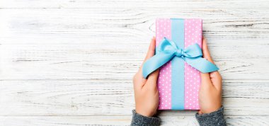 Kadın elleri renkli kağıda sarılı Noel veya diğer tatil hediyelerini verir. Hediye kutusu, hediye süsü beyaz kırsal ahşap masa, fotokopi alanı ile üst manzara.