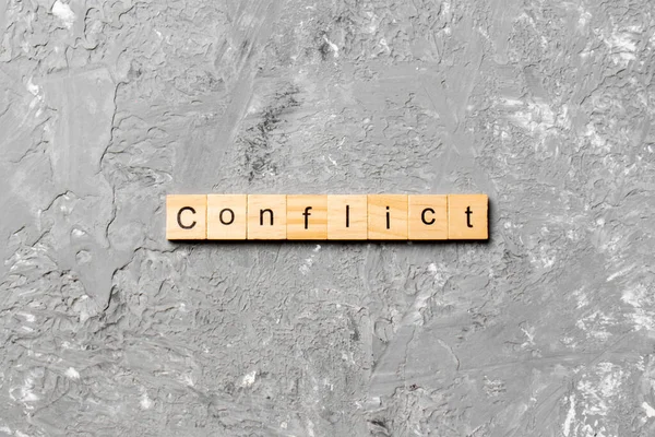Tahta bloğa yazılmış KONFLICT kelimesi. Deksing, konsept için çimento masadaki CONFLICT metin.