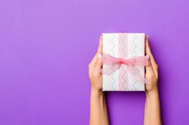 Kadınların düz uzanmış elleri hediye paketi ve dekore edilmiş mor arka planda fotokopi alanı ile. Noel ve tatil konsepti.