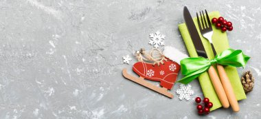 Yeni yıl yemeğinin çimento arka planındaki en iyi görüntüsü. Noel süslemeleri ve oyuncaklarıyla peçetenin üzerindeki şenlikli çatal bıçak takımı. Fotokopi alanı olan Banner aile bayramı konsepti.