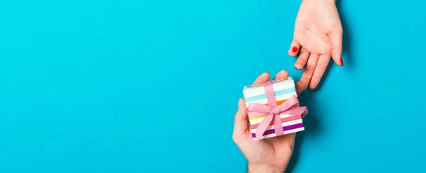 Top view of a man holding and giving a gift to a woman on colorful background. Receiving a present. Close up of holiday concept.