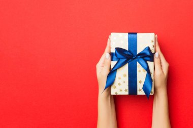 Kadının elleri kırmızı arka planda renkli kurdeleli çizgili hediye kutusunu tutuyor. Noel konsepti ya da diğer tatil el yapımı hediye kutusu, kopya alanı olan konsept üst görünüm.