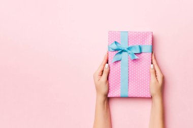 Kadının elleri çizgili hediye kutusunu tutuyor ve canlı mercan arka planında renkli kurdele var. Noel konsepti ya da diğer tatil el yapımı hediye kutusu, kopya alanı olan konsept üst görünüm.