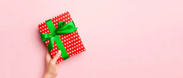 雌性的手拿着带条纹的礼品盒 在活珊瑚的背景上系上彩色丝带 圣诞概念或其他节日手工制作的礼品盒 概念顶视图与复制空间 — 图库照片