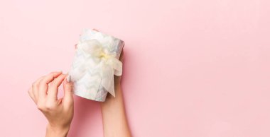 Kadının elleri çizgili hediye kutusunu tutuyor ve canlı mercan arka planında renkli kurdele var. Noel konsepti ya da diğer tatil el yapımı hediye kutusu, kopya alanı olan konsept üst görünüm.