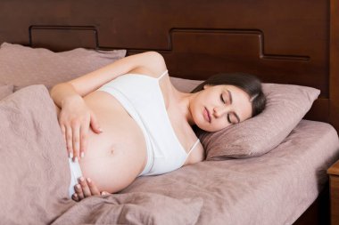 Genç, güzel hamile bir kadın, acı içinde, yatak odasında oturuyor, doğum yapmaya hazırlanıyor..