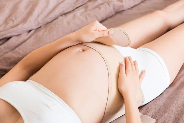 Zbliżenie Kobieta Ciąży Ubiera Bandaż Brzuchu Domu Łóżku Ortopedyczny Pas — Zdjęcie stockowe