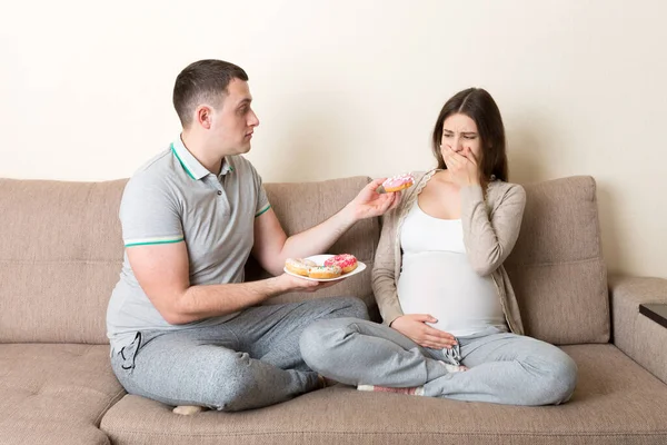 남편은 아내에게 도넛을 권하지만 아내는 거부하고 아프다는 이유로 행동을 임신중에 — 스톡 사진