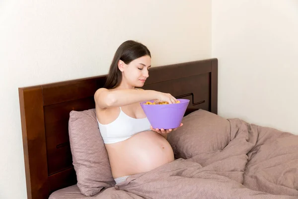 침대에서 휴식을 취하는 임신부는 소금에 욕구때문에 과자를 기간중의 불건전 정크푸드 — 스톡 사진