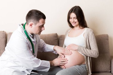 Doktor evde hamile bir kadının karnına dokunup kontrol ediyor..