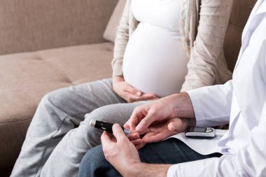 Genç doktor evde hamile bir kadının kan şekerini kontrol ediyor..