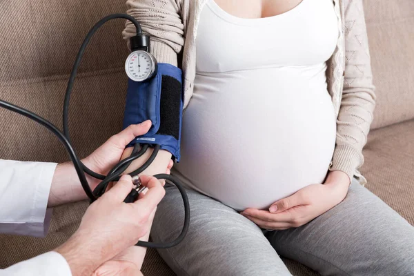 Young doctor is checking blood pressure of pregnant woman at home. High pressure problem during pregnancy concept.