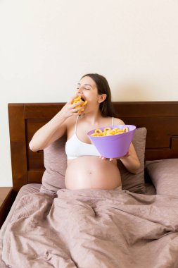 Hamile bir kadının yatakta dinlenmesi tuzlu arzular yüzünden cips yemesidir. Hamilelik sırasında sağlıksız abur cubur.