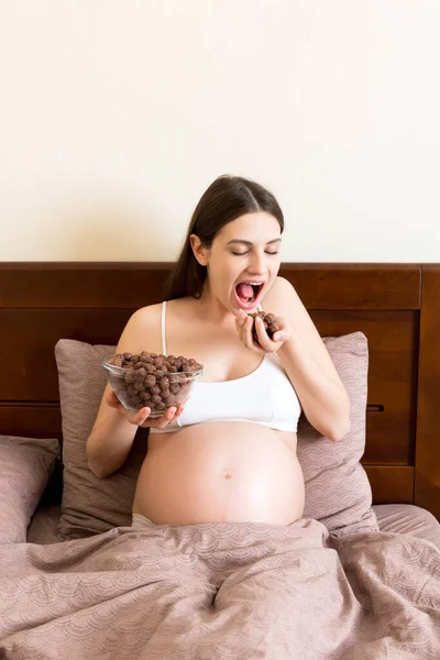 Hamile Bir Kadın Yatakta Gevşeyen Bir Kaseden Gevrek Çikolata Gevreği — Stok fotoğraf