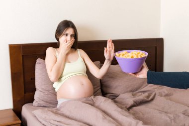 Yatakta kalan hamile kadın sağlıksız atıştırmalıklar yemeyi reddediyor. Hamilelik konseptinde abur cubur yemeyi bırak..