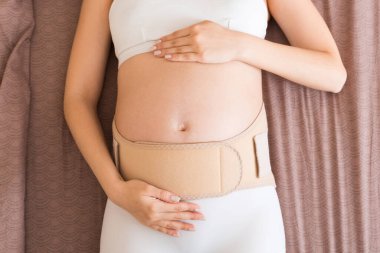 Yakın plan hamile kadın evde karnına bandaj sargılar. Ortopedik karın destek kemeri.