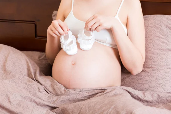 Evde Yatağında Bebek Ayakkabıları Olan Hamile Bir Kadın — Stok fotoğraf
