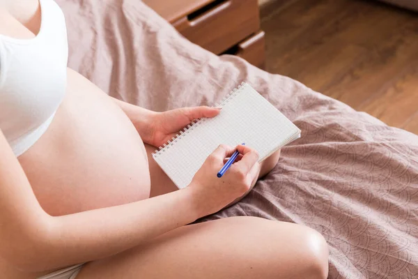 Pregnant woman makes notes in notebook. Concept of pregnancy Mother waiting for baby.