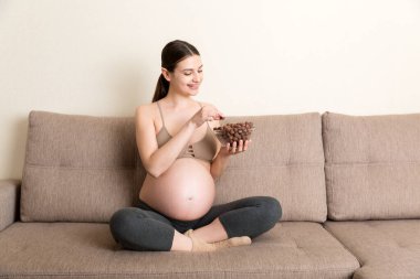 Hamile kadın koltukta gevşeyen bir kaseden gevrek çikolata gevreği yemekten hoşlanıyor. Hamilelik konsepti sırasında diyet.