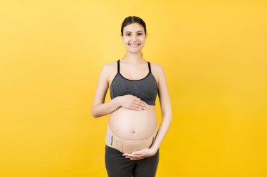 Sarı arkaplandaki hamile kadının destekleyici portresi ve fotokopi alanı. Ortopedik abdominal destek kemeri kavramı.