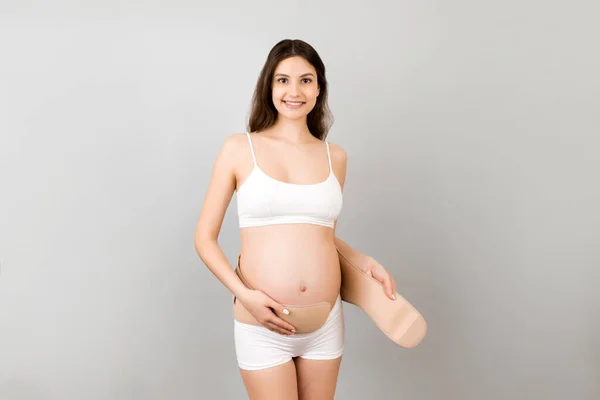 白い下着を着た妊婦の肖像画コピースペースとグレーの背景にベルトを身に着けている 腰痛に対するサポートベルト 整形外科腹部サポートベルトコンセプト — ストック写真