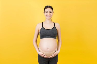 Sırtındaki ağrıyı azaltmak için arka planda fotokopi çekerek doğum kemeri takan hamile kadının portresi. Ortopedik abdominal destek kemeri kavramı.