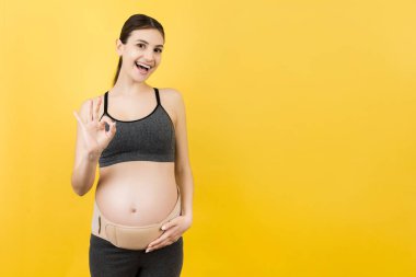 Üçüncü üç aylık dönemde hamile bir kadının portresi hamilelik kemeri takıyor ve sarı arka planda iyi olduğunu gösteriyor. Kopya alanı ile ortopedik abdominal destek kemeri kavramı.