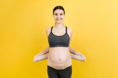 Hamile kadının portresi, arka plandaki ağrıya karşı annelik kemeri takıyor ve arka planda fotokopi çekiyor. Ortopedik abdominal destek kemeri kavramı.