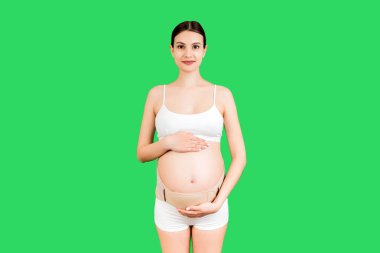 Yeşil arka planda fotokopi aletiyle sırt ağrısını azaltmak için hamile kadın iç çamaşırı giymiş elastik annelik bandı portresi. Ortopedik abdominal destek kemeri kavramı.
