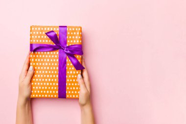 Kadının elleri çizgili hediye kutusunu tutuyor ve canlı mercan arka planında renkli kurdele var. Noel konsepti ya da diğer tatil el yapımı hediye kutusu, kopya alanı olan konsept üst görünüm.