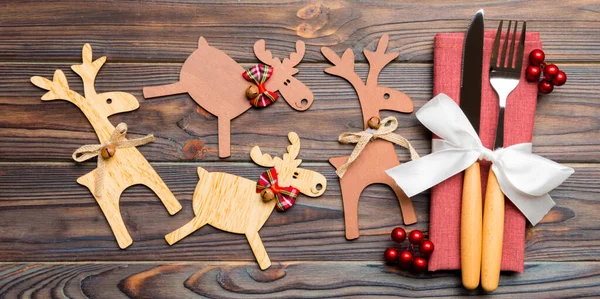 Top view of holiday objects on wooden background. Utensils tied up with ribbon on napkin. Close up of christmas decorations and reindeer. New year dinner concept.