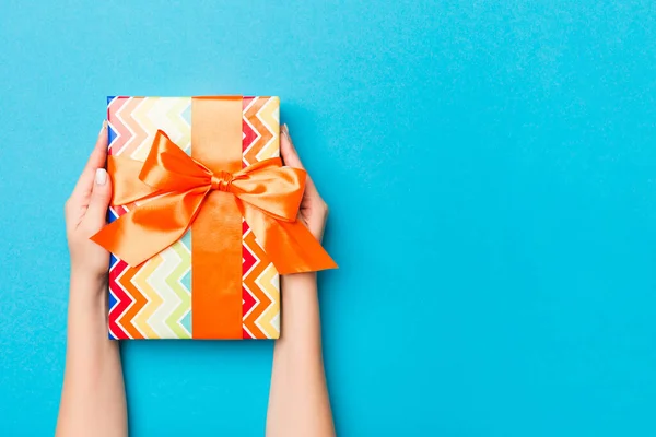 Woman arms holding gift box with colored ribbon on blue table background, top view and copy space for you design.