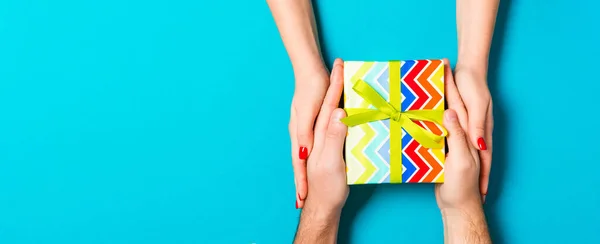 Top view of giving and receiving a gift on colorful background. Present in male and female hands. Love concept. Close up.