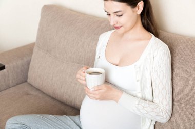 Elinde kahve fincanıyla kanepede oturan hamile bir kız. doğum sabahı.