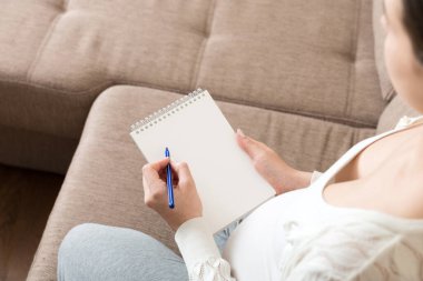 Hamile kadın notlar alır. Hamilelik, sağlık, tıp kavramı. Anne evde bebek bekliyor..