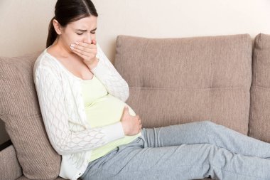 Hamilelik Sabah Hastalığı. Hamile kadın evdeki koltukta midesi bulanıyor..