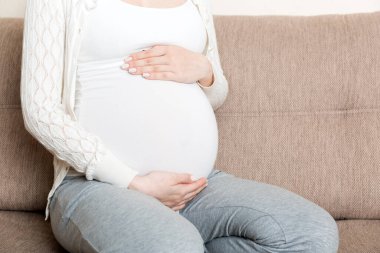 Müstakbel tatlı beyaz annenin oturma odasında kanepede uzanmış ve karnının üstünde el ele tutuşurken fotoğrafı..