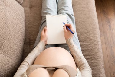 Hamile kadın notlar alır. Hamilelik, sağlık, tıp kavramı. Anne evde bebek bekliyor..