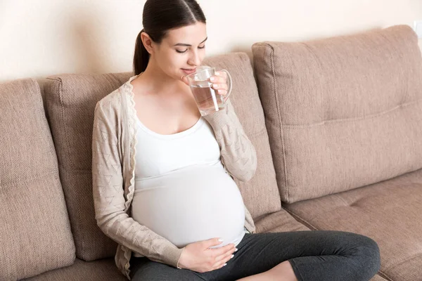 Έγκυος Γυναίκα Ένα Ποτήρι Νερό Κάθεται Στον Καναπέ Στο Σπίτι — Φωτογραφία Αρχείου