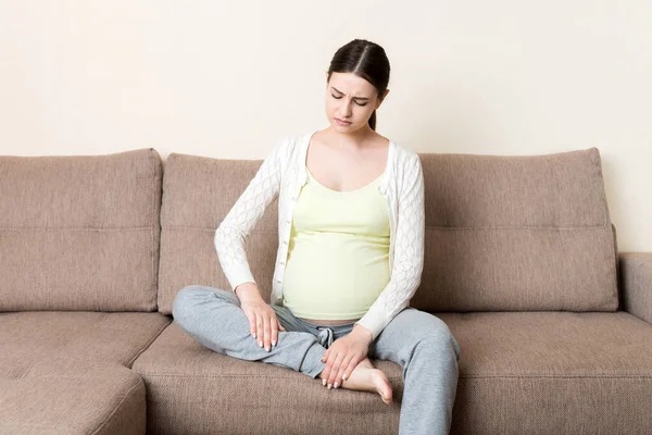 Leg cramps during pregnancy. Closeup of hands massaging swollen foot while sitting on sofa. — Stock Image Leg Cramps Pregnancy Closeup Hands Massaging Swollen Foot While Sitting Royalty Free Stock Images