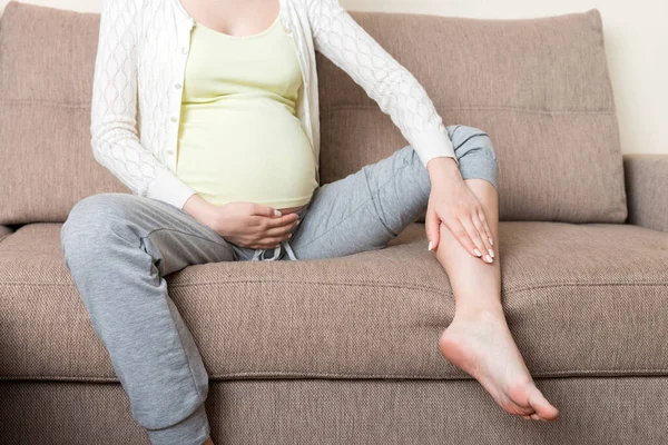 Leg cramps during pregnancy. Closeup of hands massaging swollen foot while sitting on sofa. — Stock Image Leg Cramps Pregnancy Closeup Hands Massaging Swollen Foot While Sitting Royalty Free Stock Photos