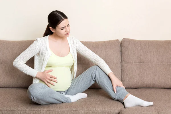 Leg cramps during pregnancy. Closeup of hands massaging swollen foot while sitting on sofa. — Stock Image Leg Cramps Pregnancy Closeup Hands Massaging Swollen Foot While Sitting Stock Photo