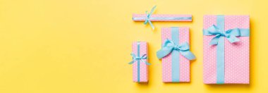 Sarı arka planda mavi kurdeleli kağıtlara sarılmış Noel ya da diğer tatil hediyeleri. Hediye kutusu, hediye dekorasyonu renkli masa, üst görünüm.