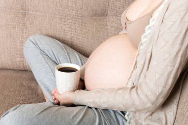 Elinde kahve fincanıyla kanepede oturan hamile bir kız. doğum sabahı.