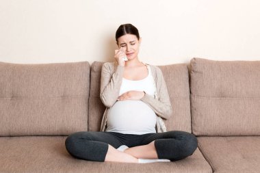 Evdeki kanepede ağlayan hamile bir kadın..