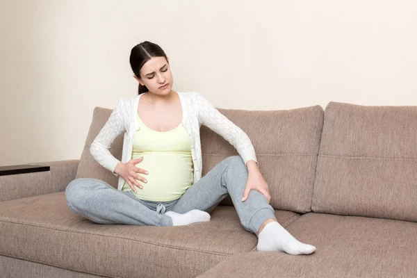Leg cramps during pregnancy. Closeup of hands massaging swollen foot while sitting on sofa. — Stock Image Leg Cramps Pregnancy Closeup Hands Massaging Swollen Foot While Sitting Stock Photo